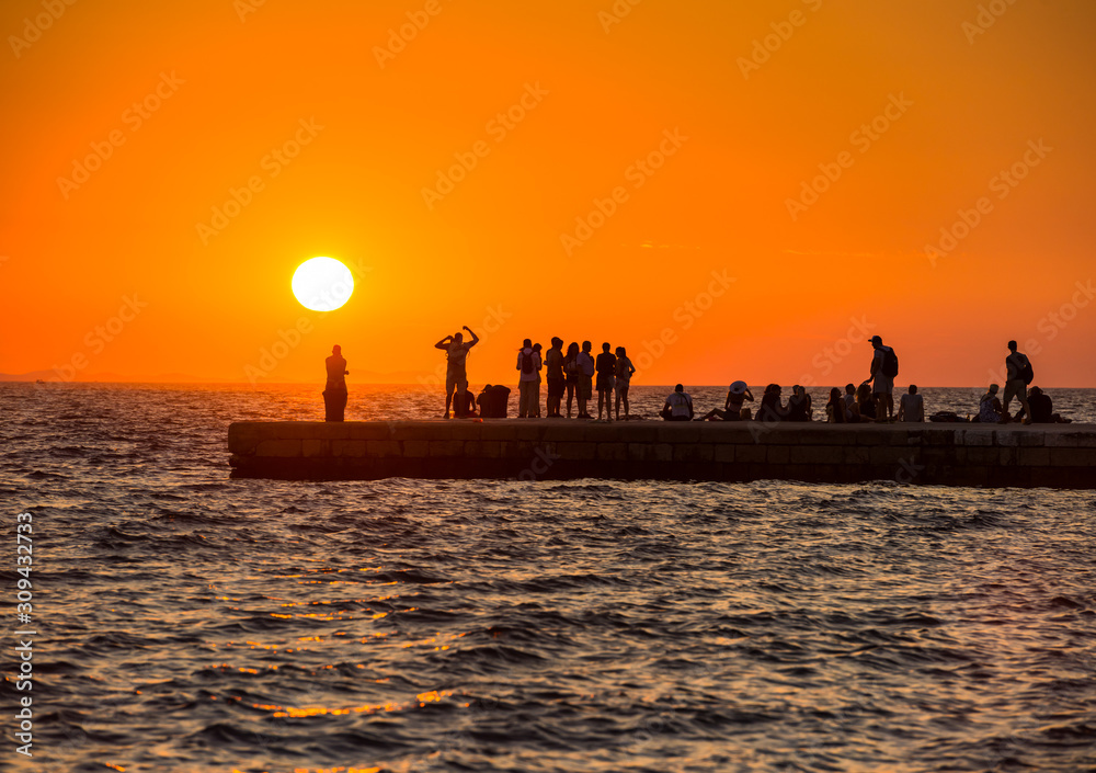 Sunset silhouettes of the people on the pier with setting sun and orange sky in Croatia