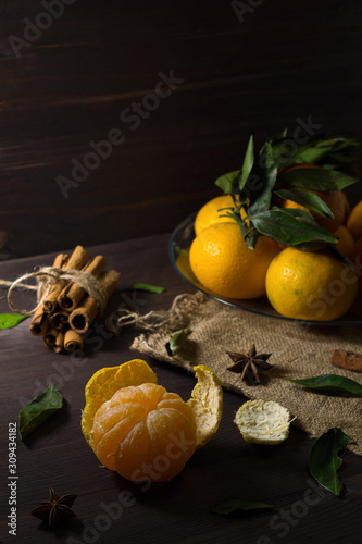 ripe mandarin on wooden table. Fresh orange tangerines with green leaves in a glass plate on a dark wooden background with spices. low key.