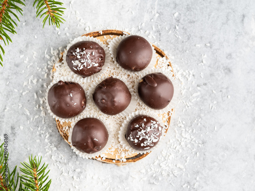 Winter dessert, healthy sugarfree peanut butter truffles covered by dark chocolate and coconut shred, christmas and new year background, fir tree branches, wooden plate, white background