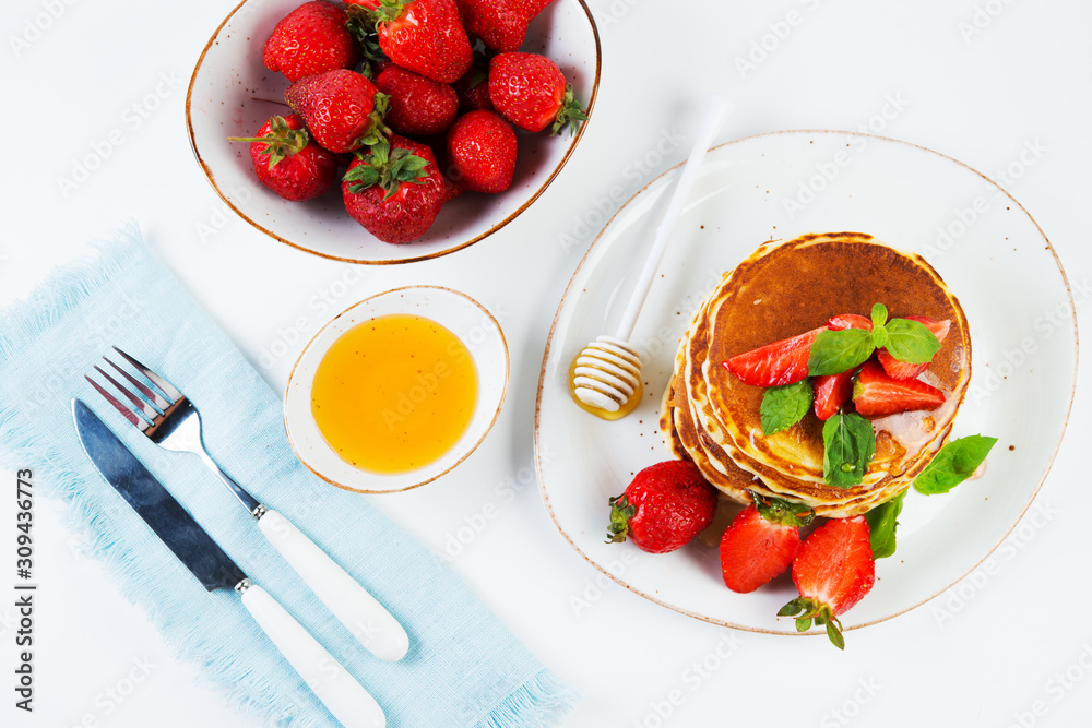 American pancakes lined with strawberries and honey poured on a white background. Classic American Breakfast. Top view American pancakes lined with strawberries and honey poured on a white background. Classic American Breakfast. Top view