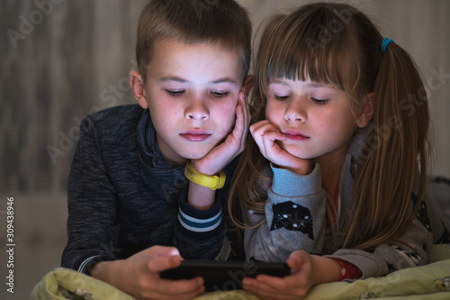Two children brother and sister watching video on smartphone screen together.