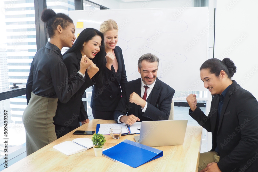 Group of multinational people working together in the office looking at their laptop after getting work done successfully. All smiling and feeling excited with lifestyle and happy workplace concept