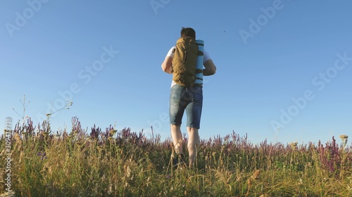 Young male traveler goes uphill in a field with beautiful flowers. Travel and adventure concept. tourist travels in nature, with a backpack climbs a hill. healthy lifestyle concept
