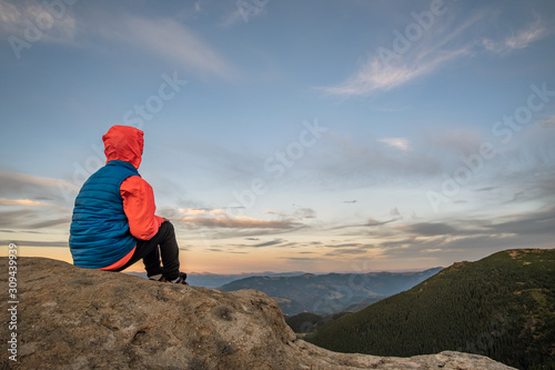 Young child boy hiker sitting in mountains enjoying view of amazing mountain landscape.
