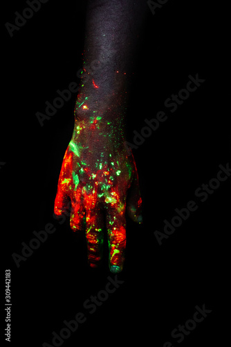 Male hand painted with fluorescent paint glowing in the darkness