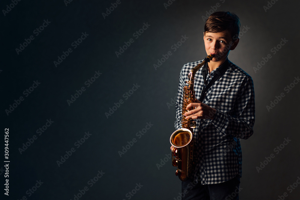 Naklejka premium A boy on a dark background with a searchlight plays saxophone