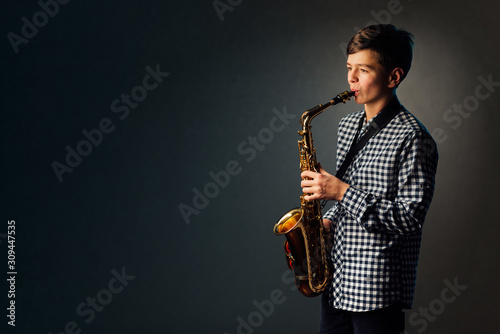 Canvas Print A boy on a dark background with a searchlight plays saxophone