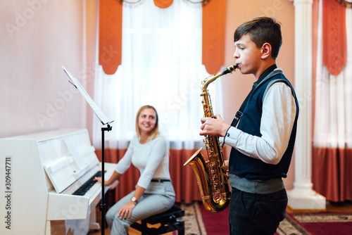 A student boy in a saxophone lesson learns to play accompaniment of a cheerful teacher on the piano