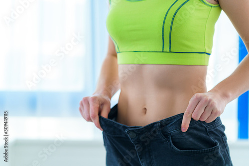Healthy sport fitness slim woman pulling her large jeans and showing weight loss and diet results. Motivation and progress in slimming