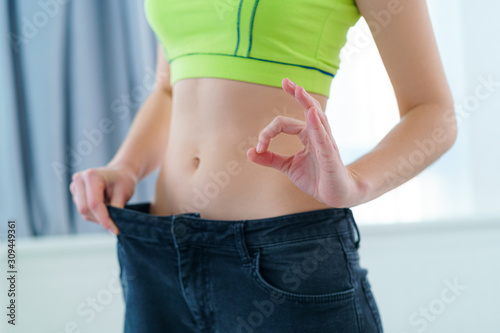 Healthy sport fitness woman with slim waist pulling her big jeans and showing losing weight results. Goal achievement, motivation and progress in slimming and diet