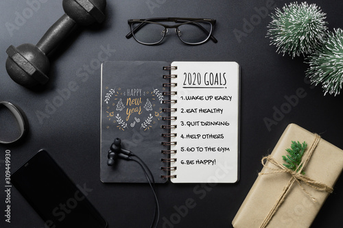 New Year Healthy Goals and Resolutions concept. 2020 New Year's Goals written on Notebook Paper, and dumbbells on black Background, Fitness, Sport and Health Concept, Top View