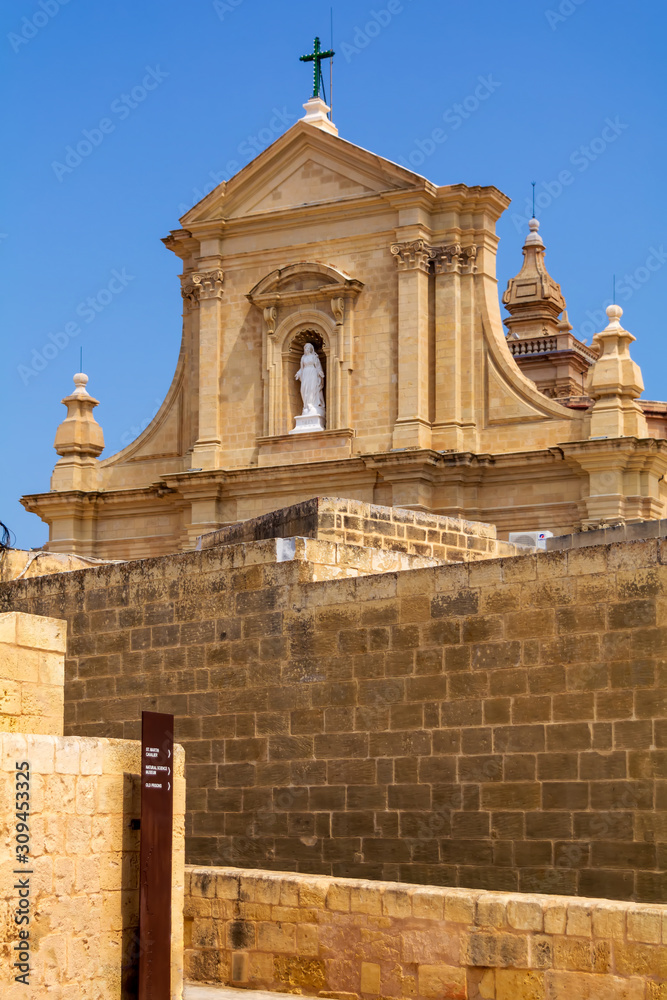 Obraz premium Facade of the Cathedral of the Assumption behind massive walls of the Cittadella of Victoria in Gozo, Malta. Cathedral is a fine baroque structure and is built entirely from local limestone.