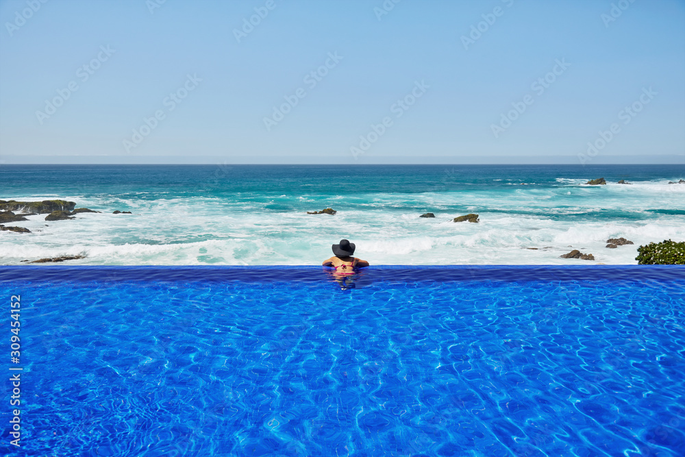 Woman looking at the ocean from infinity pool at luxury resort Woman looking at the ocean from infinity pool at luxury resort