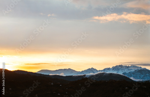 Dawn landscape on a background of snowy mountains in the fog early in the morning © Goffkein