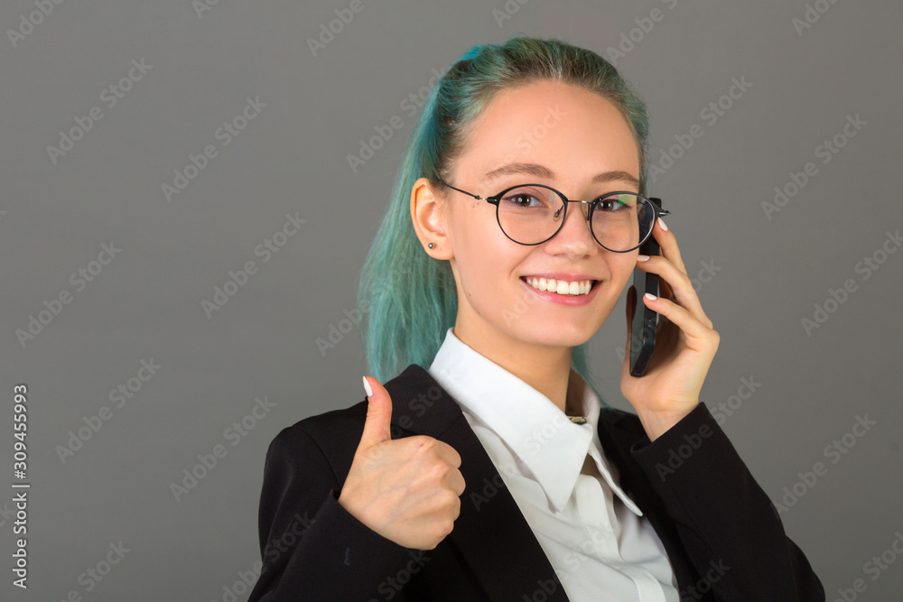 beautiful young woman in glasses and a black suit on a gray background with a phone in his hand beautiful young woman in glasses and a black suit on a gray background with a phone in his hand