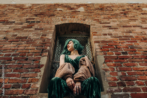 Beautiful woman with green hair sitting on a ledge of a brick wall building outside in the city photo