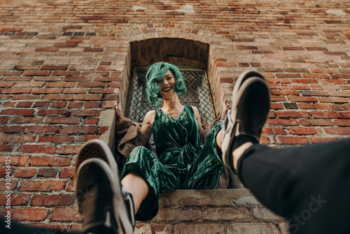 Beautiful woman laughing with green hair sitting on a ledge of a brick wall building outside in the city photo