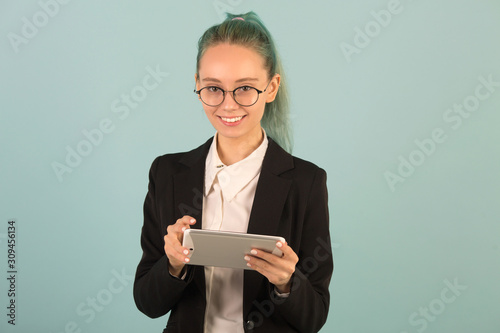 beautiful young woman in glasses and a black suit on a gray background with a tablet in hand