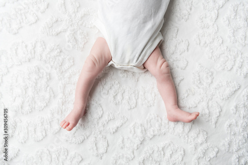 A faceless baby laying on a white chenille blanket in a white onesie photo