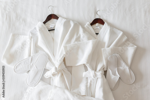 two white bathrobes and slippers on the bed in hotel room