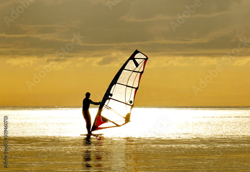 Windsurfing in the rays of the setting sun. Silhouette of a man on a golden background. photo