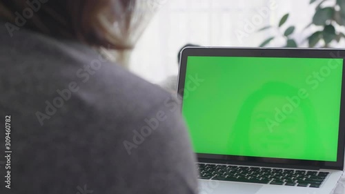 Over the shoulder shot of Asian woman looking at green screen. Office person using laptop computer with laptop green screen, 4K dolly shot