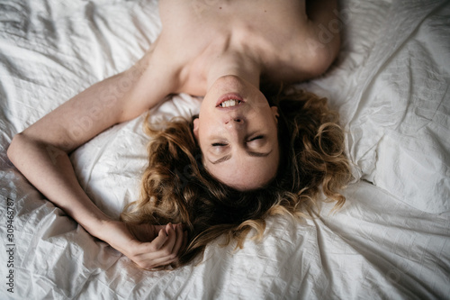 Young naked seductive woman feeling sexual ecstasy while lying on a bed photo