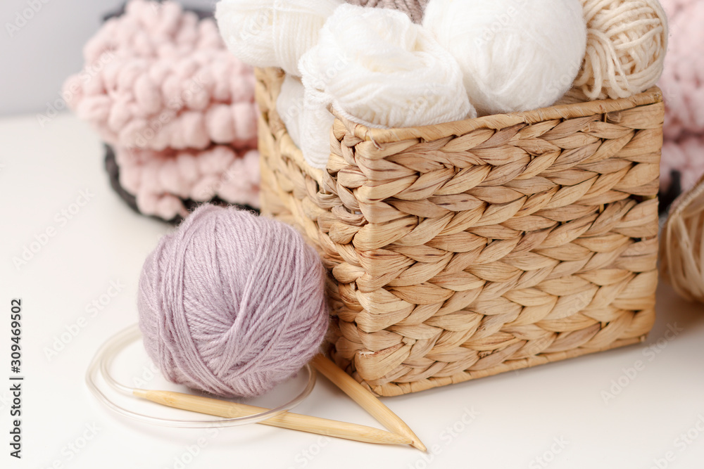 Wooden knitting needles and balls of yarn in wicker basket on light background. Concept of hobby. Handicraft