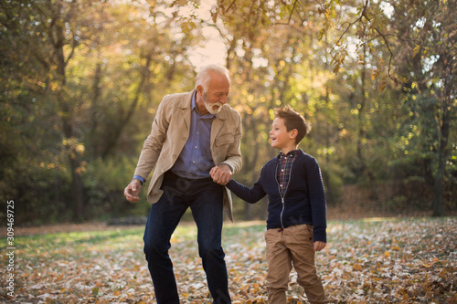 Schilderij op canvas A grandfather and his grandson strolling around the park, talking and holding hands