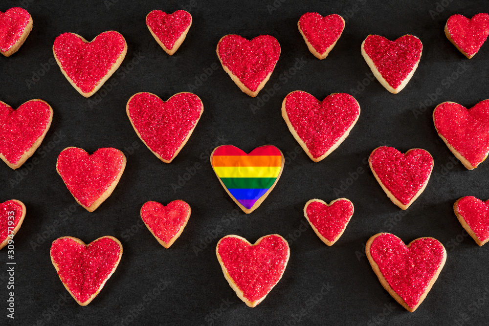 Red and rainbow colored heart shaped cookies on black background, distinction concept, love symbol