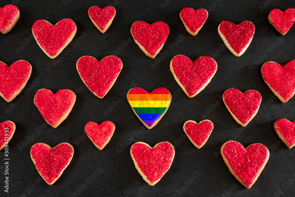 Red and rainbow colored heart shaped cookies on black background, distinction concept, love symbol Red and rainbow colored heart shaped cookies on black background, distinction concept, love symbol