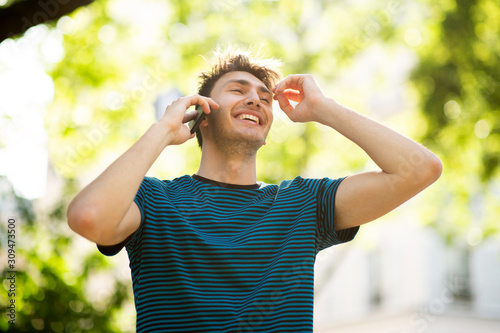 smiling young man talking with phone outdoors in park