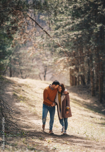 Young beautiful couple in love walking embraced through forest in the autumn.