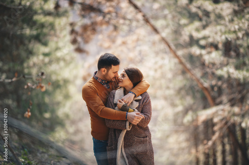 Beautiful couple in love looking each other and embracing while they are standing in the forest.