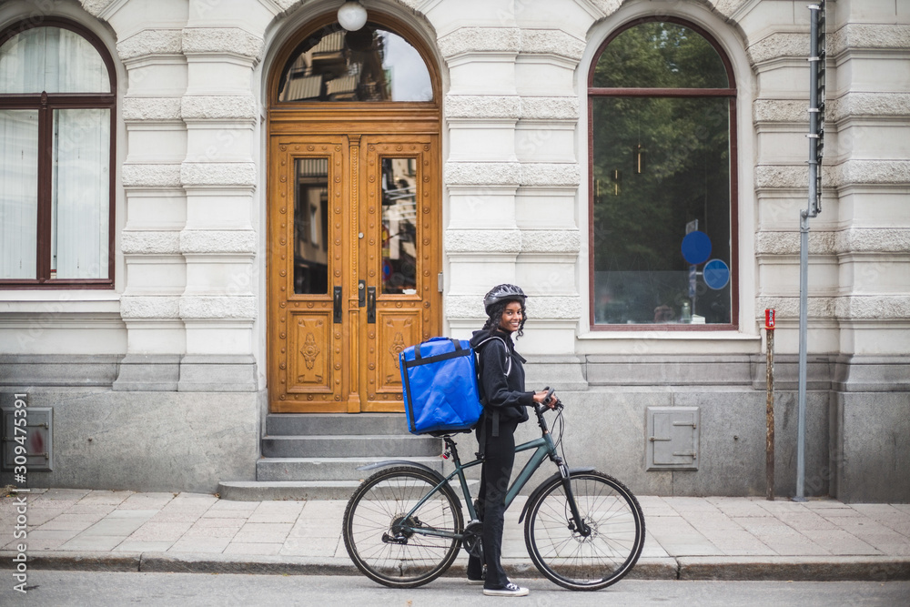 Side view portrait of smiling delivery woman with bicycle on street in city Side view portrait of smiling delivery woman with bicycle on street in city