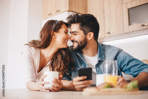 Fotografi A woman holding a mug  about to kiss her husband in the kitchen