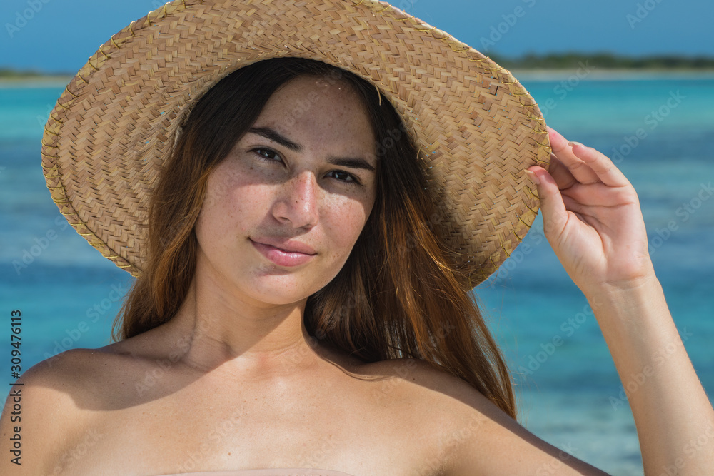 Portrait of happy young latin woman smiling with beach hat on tropical beach.  