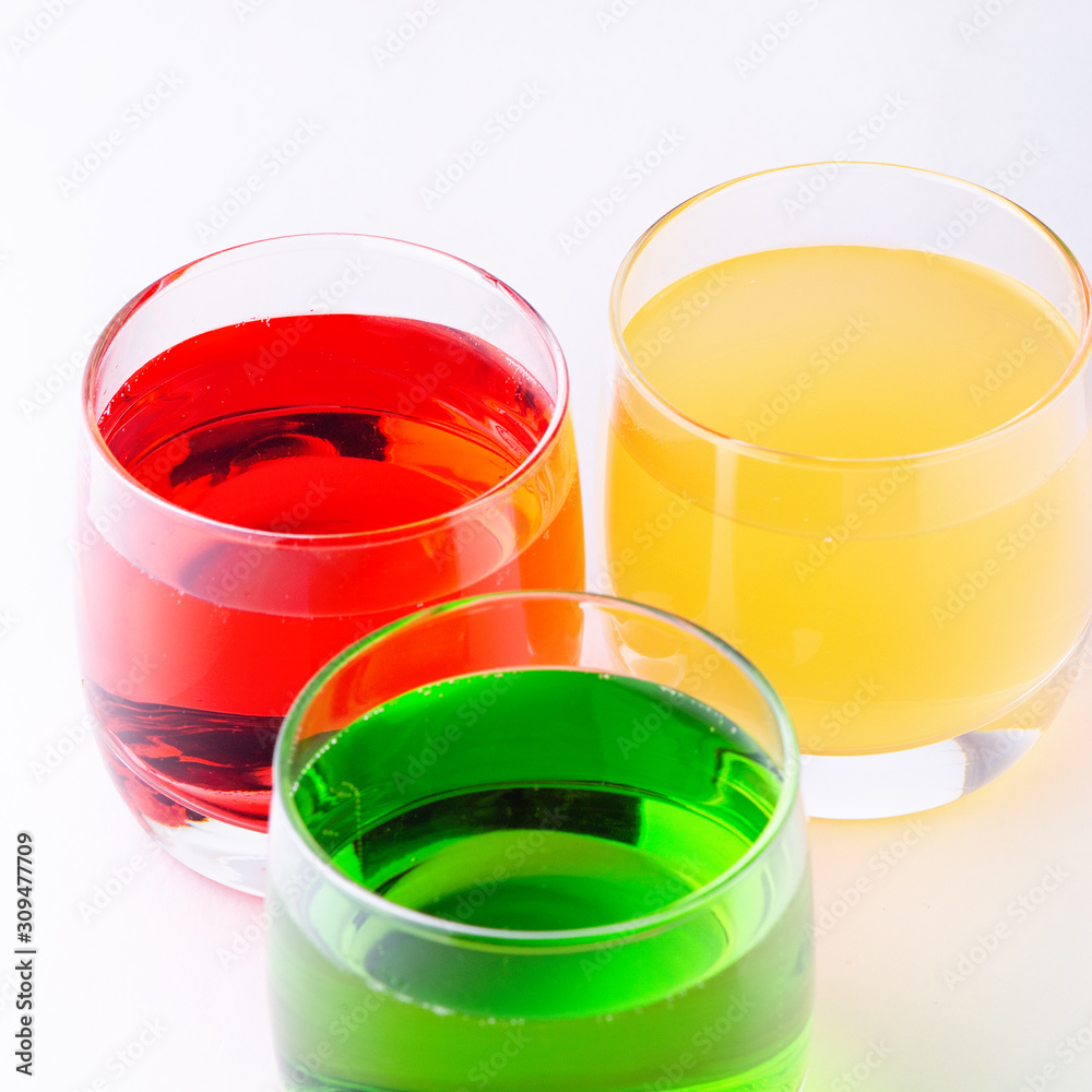 Glasses of various colors and tastes soda drink on white background. Red, yellow, green soda or sparkling water close up on white table, copy space Glasses of various colors and tastes soda drink on white background. Red, yellow, green soda or sparkling water close up on white table, copy space