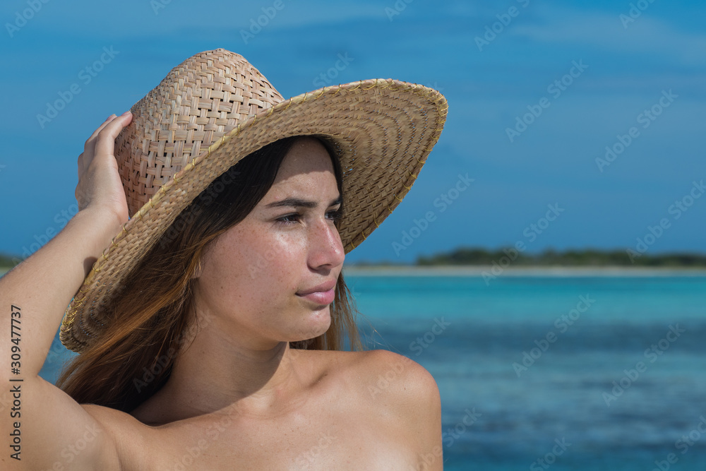 Portrait of young woman in sunny day with hat looking right at blue water sea tropical beach. 