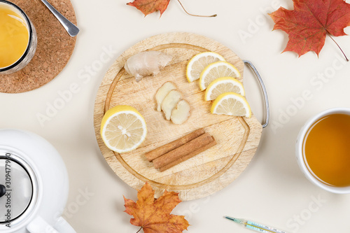 Close up photo of wooden platter with lemon  ginger and cinnamon sticks. Near bowl of honey  teapot  a cup of tea and thermometer. Natural remedies for flu and colds. Winter season concept. Flat lay.