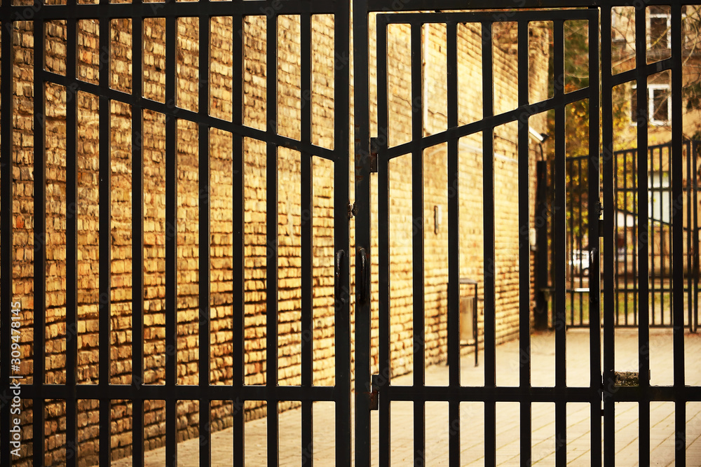 Closed metal entrance gate on brick wall background Closed metal entrance gate on brick wall background