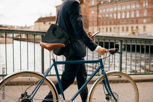 Midsection of businessman using smart phone while walking with bicycle on bridge in city