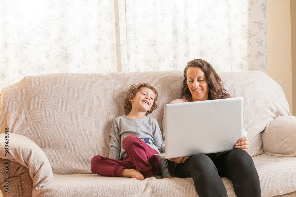 Child and woman sitting on a sofa watching a laptop.