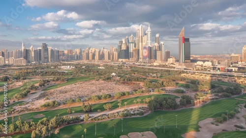 Dubai Marina with JLT skyscrapers and golf course morning timelapse, Dubai, United Arab Emirates. Aerial view from Greens district. Green lawn and cloudy sky photo