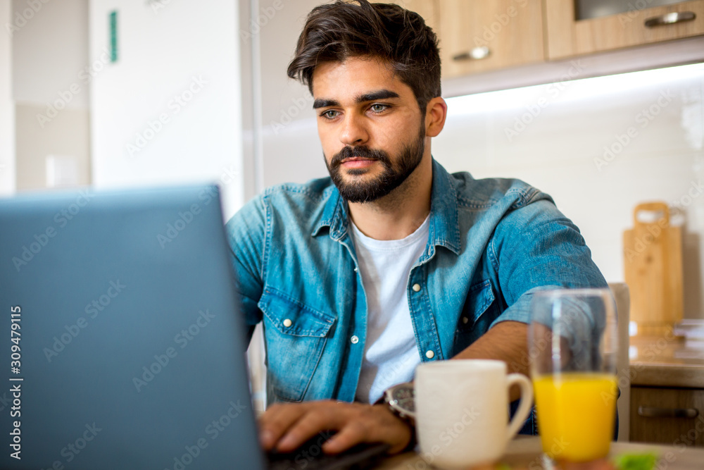 Young handsome bearded Caucasian man chatting with his friends on his laptop while he's having a cup of coffee and glass of juice. Young handsome bearded Caucasian man chatting with his friends on his laptop while he's having a cup of coffee and glass of juice.