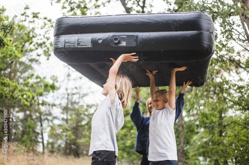 Siblings carrying inflatable mattress walking at camping site