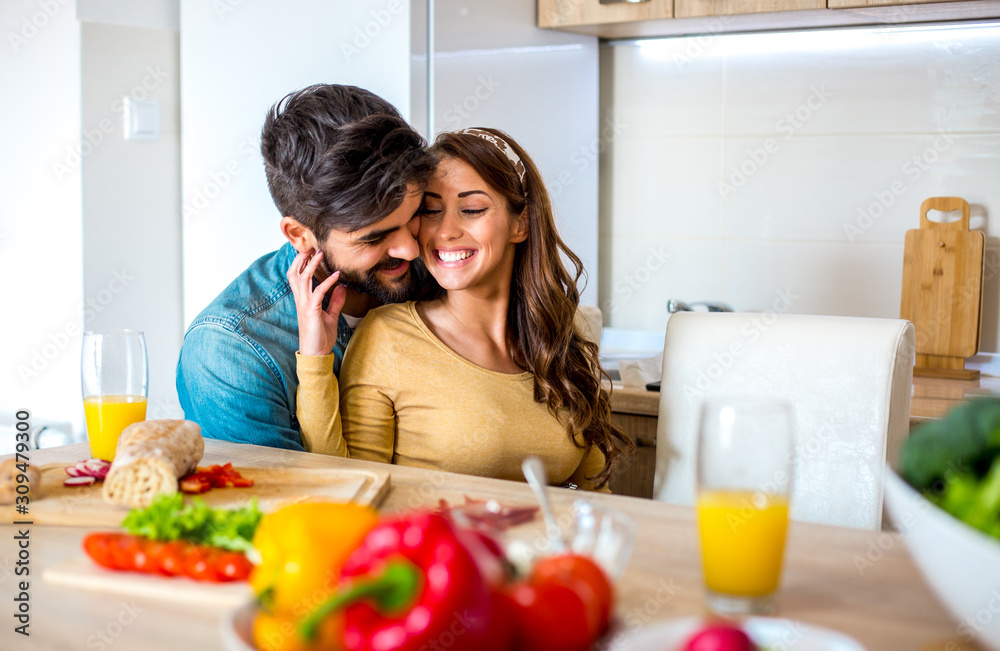 Young cute Caucasian couple embracing with love and affection during brunch in the kitchen.