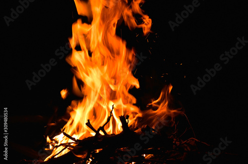 in the photo of a dark night, a yellow-red flame burns, firewood is visible from below