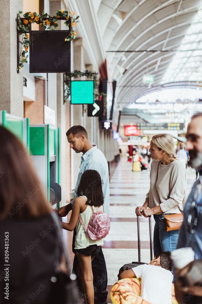 Man with family buying tickets from automated machine at train station Man with family buying tickets from automated machine at train station