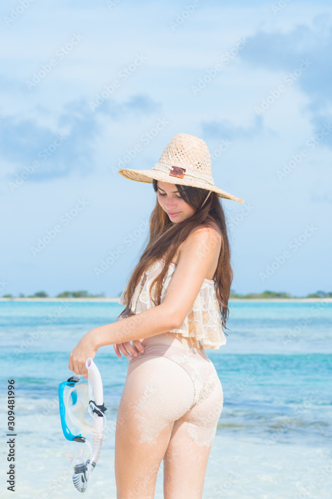 Young woman with wet skin looking down at tropical beach holding mask snorkel with hand